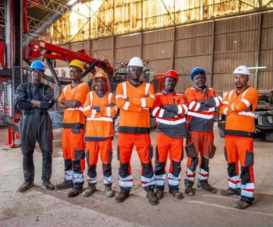 Une équipe d'une dizaine de personnes en tenue haute visibilité orange et casques de chantier, alignée devant un bâtiment industriel.