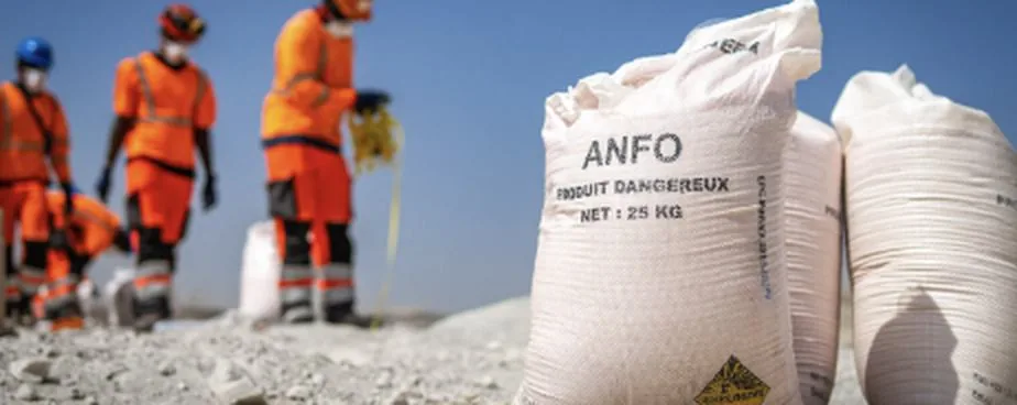 Un opérateur en tenue haute visibilité orange prélève du produit dans un grand sac blanc, sur une aire de chargement.